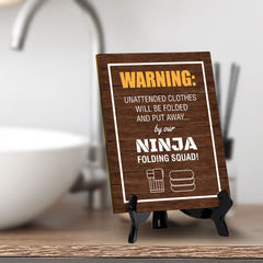 Signs ByLITA Warning: Unattended clothes will be folded and put away... by our ninja folding squad! Table Sign with Acrylic Stand (6x8“)